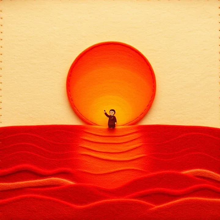 Felt and wool illustration: A glowing sun rising over a flat ocean, with a small figure of God pointing toward it. Bright red and orange colors.